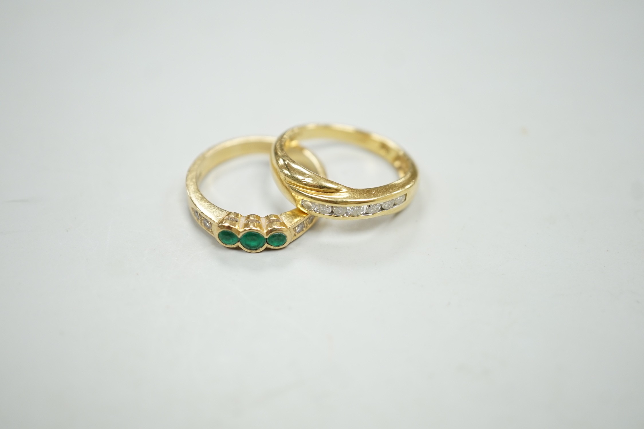 A modern 18ct gold and cannel set seven stone diamond crossover ring, size O and a similar 18k, three stone emerald and four stone diamond chip set ring, size N/O, gross weight 7.8 grams.